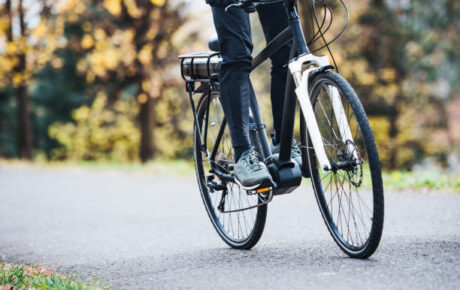 An unrecognizable man on an electrobike cycling outdoors on a road in park.